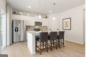 kitchen featuring a kitchen island with sink, stainless steel appliances, white cabinetry, light countertops, and decorative light fixtures