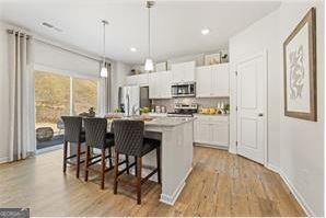 kitchen with light countertops, appliances with stainless steel finishes, white cabinetry, an island with sink, and a kitchen breakfast bar