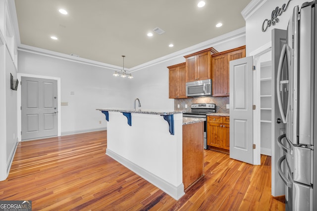 kitchen with an island with sink, stainless steel appliances, a breakfast bar, crown molding, and light hardwood / wood-style flooring