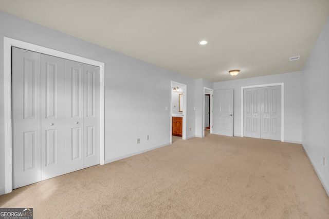 unfurnished bedroom with light colored carpet, connected bathroom, and multiple closets