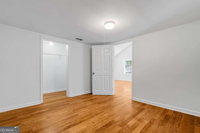 unfurnished bedroom featuring a spacious closet, a closet, and light wood-type flooring