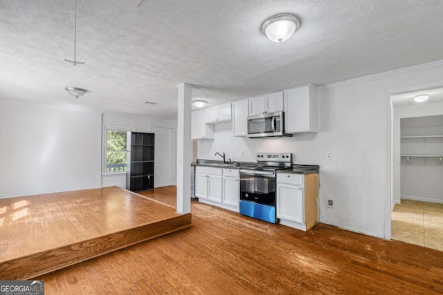 kitchen with white cabinets, hardwood / wood-style flooring, sink, appliances with stainless steel finishes, and a textured ceiling