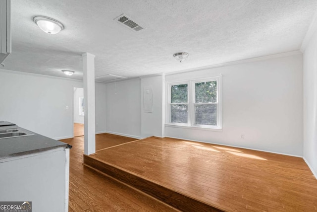 unfurnished room featuring hardwood / wood-style flooring, sink, ornamental molding, and a textured ceiling