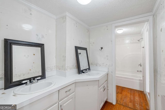 bathroom featuring vanity, ornamental molding, wood-type flooring, a textured ceiling, and washtub / shower combination