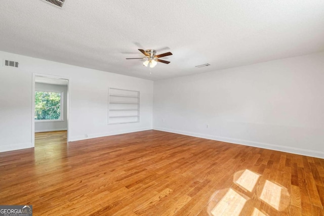 unfurnished room with ceiling fan, a textured ceiling, built in features, and hardwood / wood-style floors