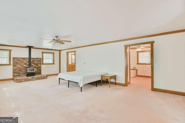 bedroom with a wood stove, ornamental molding, light colored carpet, and ceiling fan