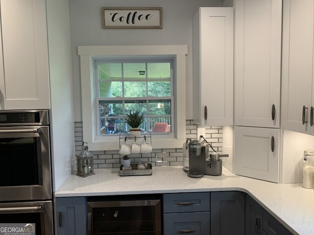 kitchen featuring beverage cooler, light stone counters, decorative backsplash, white cabinets, and double oven