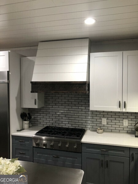 kitchen with backsplash, appliances with stainless steel finishes, premium range hood, and white cabinetry