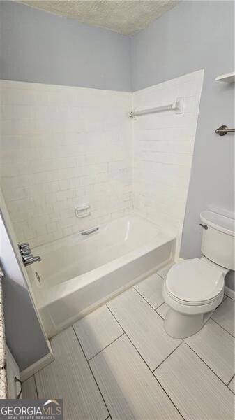 bathroom featuring toilet, tiled shower / bath combo, and a textured ceiling