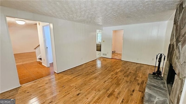 unfurnished living room with a stone fireplace, a textured ceiling, and hardwood / wood-style floors