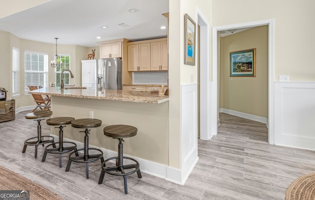 kitchen with stainless steel fridge, sink, decorative light fixtures, light hardwood / wood-style flooring, and light stone countertops