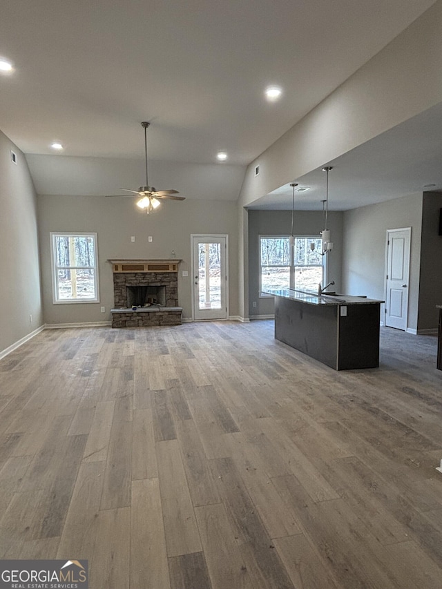 unfurnished living room with a stone fireplace, hardwood / wood-style floors, lofted ceiling, and ceiling fan