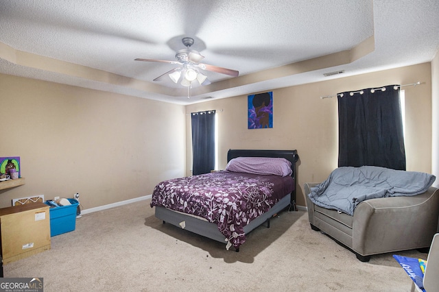 carpeted bedroom featuring a textured ceiling, a tray ceiling, and ceiling fan