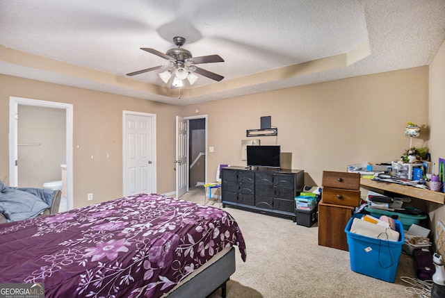 bedroom with ensuite bath, light colored carpet, a raised ceiling, a textured ceiling, and ceiling fan