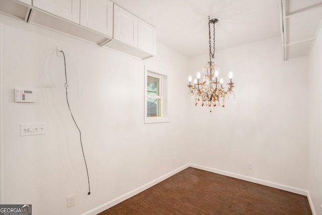 empty room with a notable chandelier and dark hardwood / wood-style floors