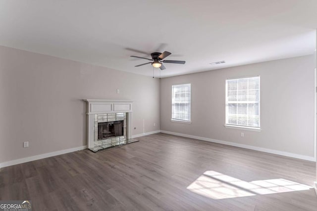 unfurnished living room with wood-type flooring, a tiled fireplace, and ceiling fan