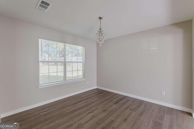 spare room featuring dark wood-type flooring and an inviting chandelier