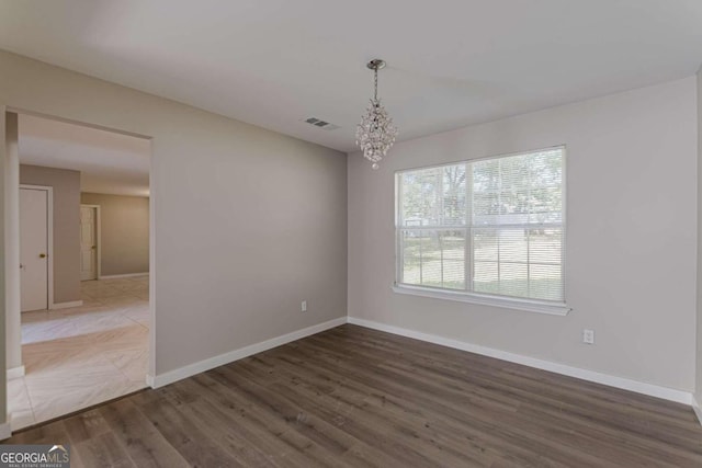 spare room featuring an inviting chandelier and dark hardwood / wood-style flooring