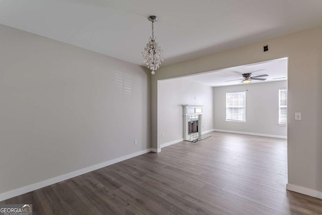 unfurnished living room with ceiling fan with notable chandelier and dark wood-type flooring