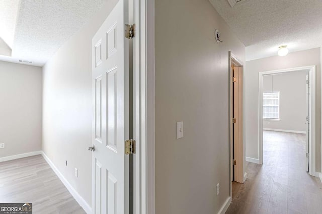 hall with light wood-type flooring and a textured ceiling