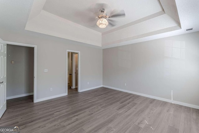 unfurnished bedroom featuring wood-type flooring, a raised ceiling, a closet, and ceiling fan