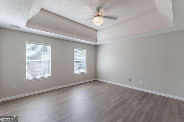 empty room featuring wood-type flooring, a textured ceiling, a tray ceiling, and ceiling fan