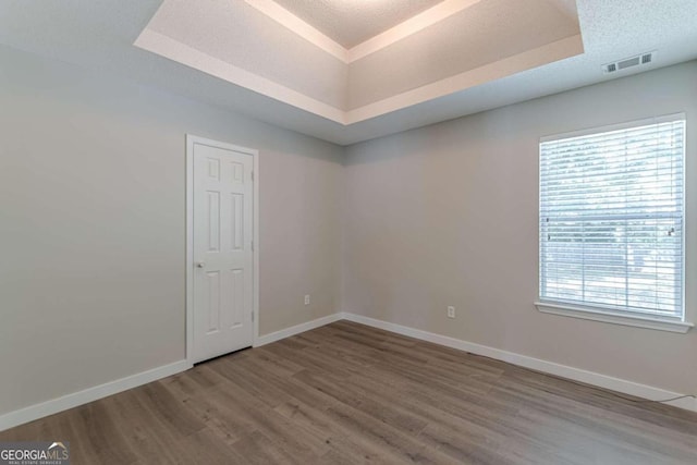 spare room with hardwood / wood-style flooring, a raised ceiling, and a textured ceiling