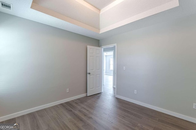 empty room featuring a tray ceiling and dark hardwood / wood-style floors