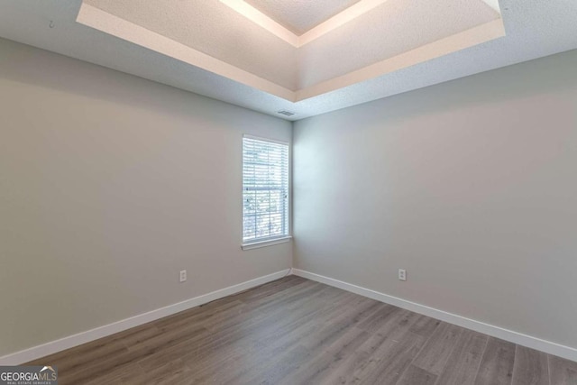 empty room with hardwood / wood-style flooring, a tray ceiling, and a textured ceiling