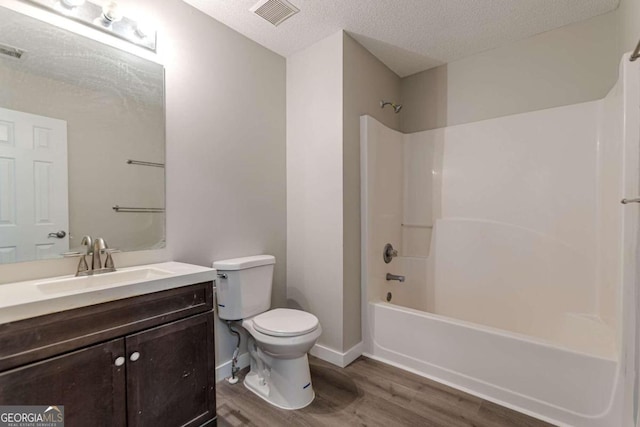 full bathroom featuring tub / shower combination, toilet, wood-type flooring, vanity, and a textured ceiling