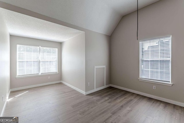 unfurnished room with a textured ceiling, lofted ceiling, and light hardwood / wood-style floors