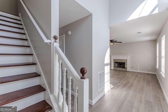 stairs with ceiling fan, a tile fireplace, and hardwood / wood-style floors