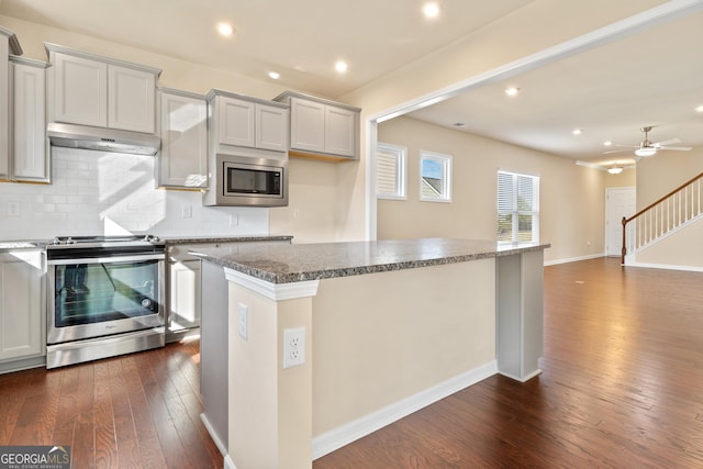 kitchen with ceiling fan, a center island, dark wood-type flooring, stainless steel appliances, and stone countertops