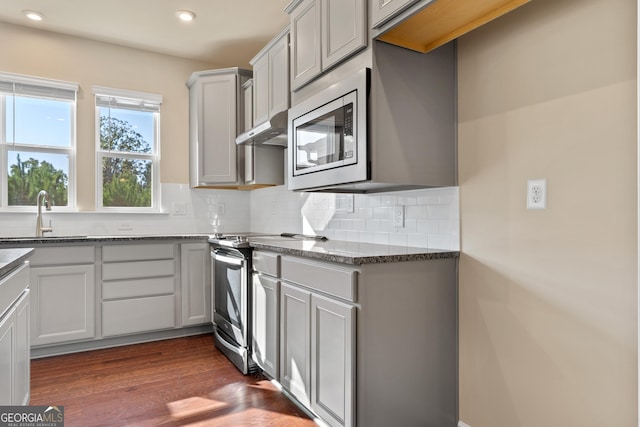 kitchen with sink, dark hardwood / wood-style flooring, dark stone counters, decorative backsplash, and appliances with stainless steel finishes