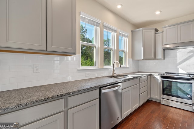 kitchen featuring sink, decorative backsplash, light stone countertops, appliances with stainless steel finishes, and dark hardwood / wood-style flooring