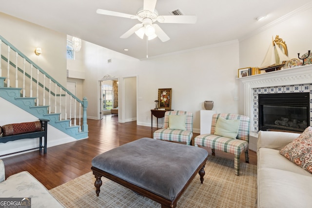 living room with ceiling fan, dark hardwood / wood-style floors, a fireplace, a towering ceiling, and crown molding