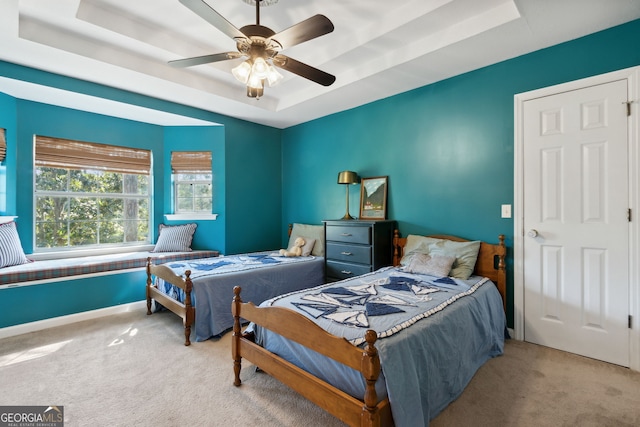 carpeted bedroom featuring ceiling fan and a raised ceiling