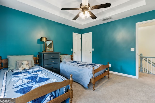 bedroom with ceiling fan, a tray ceiling, and light colored carpet