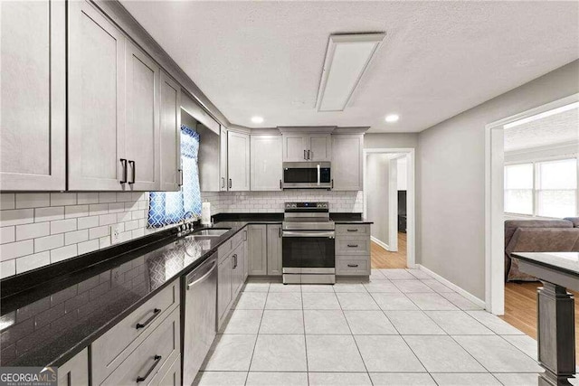 kitchen with light tile patterned flooring, gray cabinets, decorative backsplash, sink, and stainless steel appliances