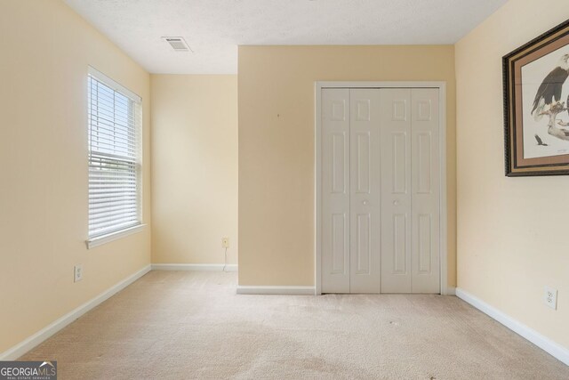 unfurnished bedroom featuring light carpet, a closet, and a textured ceiling