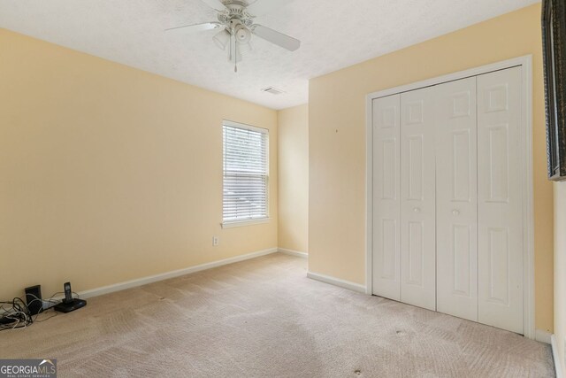 unfurnished bedroom with ceiling fan, a closet, and light carpet