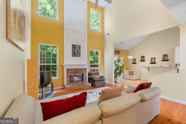 living room featuring ceiling fan, light wood-type flooring, a fireplace, and high vaulted ceiling