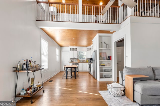 living room featuring a towering ceiling, wooden ceiling, and light wood-type flooring