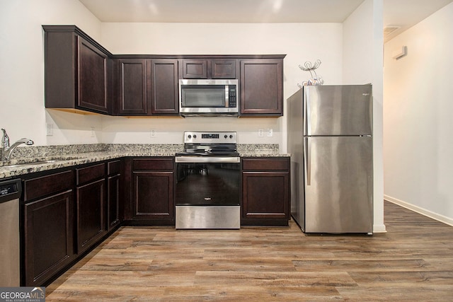 kitchen with dark brown cabinetry, light hardwood / wood-style flooring, sink, light stone counters, and appliances with stainless steel finishes