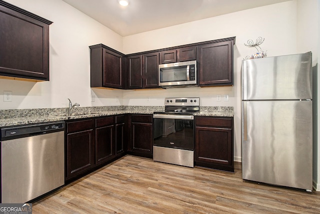 kitchen with light stone counters, stainless steel appliances, sink, light hardwood / wood-style flooring, and dark brown cabinets