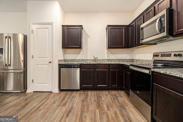 kitchen with light stone counters, dark brown cabinetry, stainless steel appliances, sink, and light hardwood / wood-style flooring