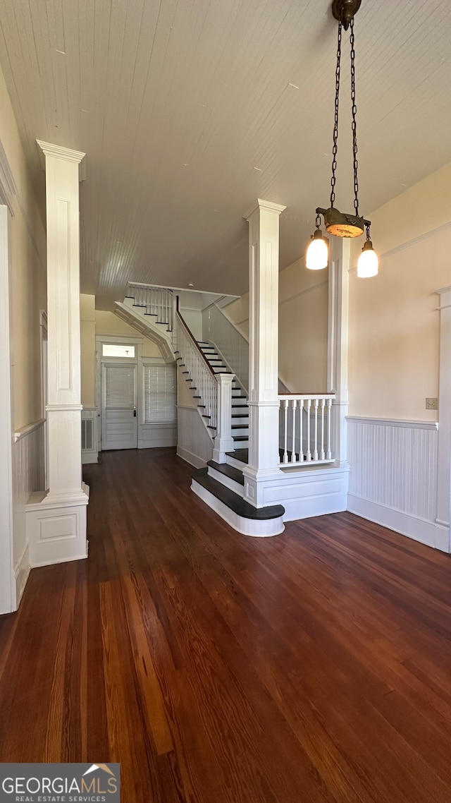 unfurnished living room featuring ornate columns and dark hardwood / wood-style flooring