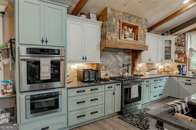 kitchen with stainless steel appliances, dark stone countertops, light wood-type flooring, white cabinets, and tasteful backsplash