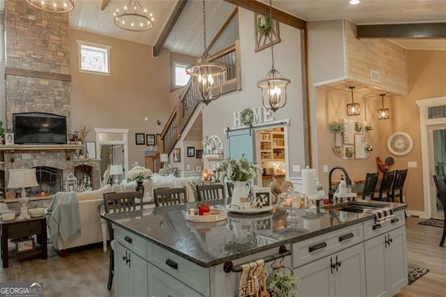 kitchen with an island with sink, dark stone countertops, pendant lighting, white cabinetry, and high vaulted ceiling