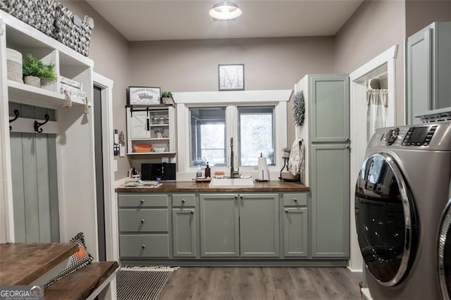 laundry room featuring sink, washer and clothes dryer, light hardwood / wood-style floors, and cabinets